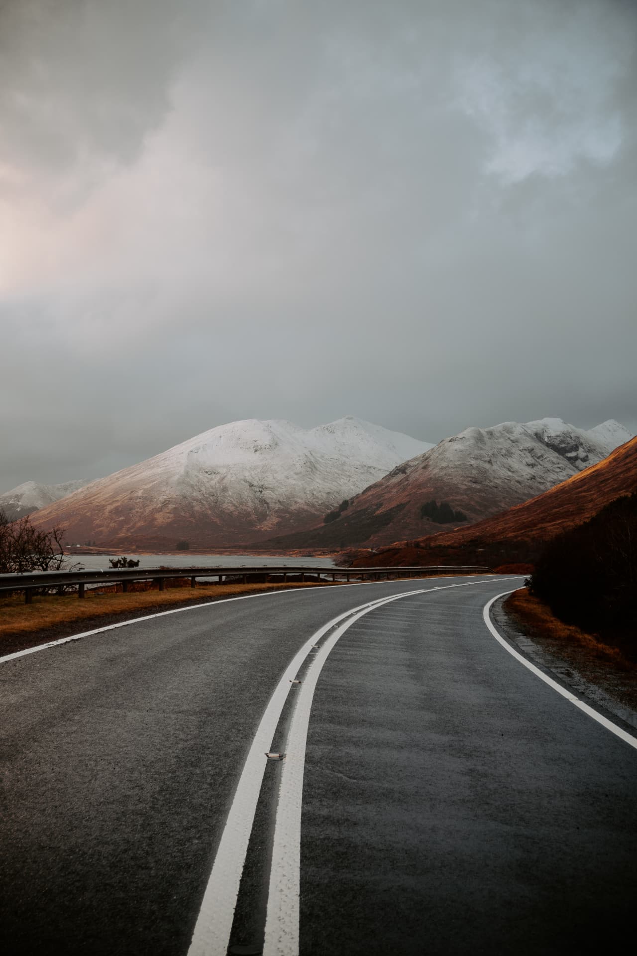 Carretera de montaña con cumbres nevadas al fondo, fotografía de paisaje por Fer Herrera