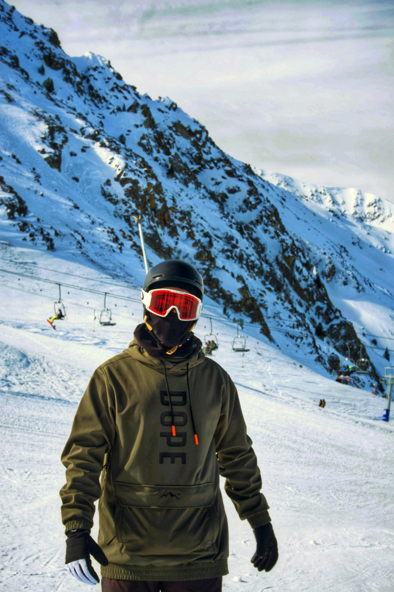 Snowboarder de pie en la pista con una telesilla y montañas nevadas de fondo, retrato de aventura por Fer Herrera