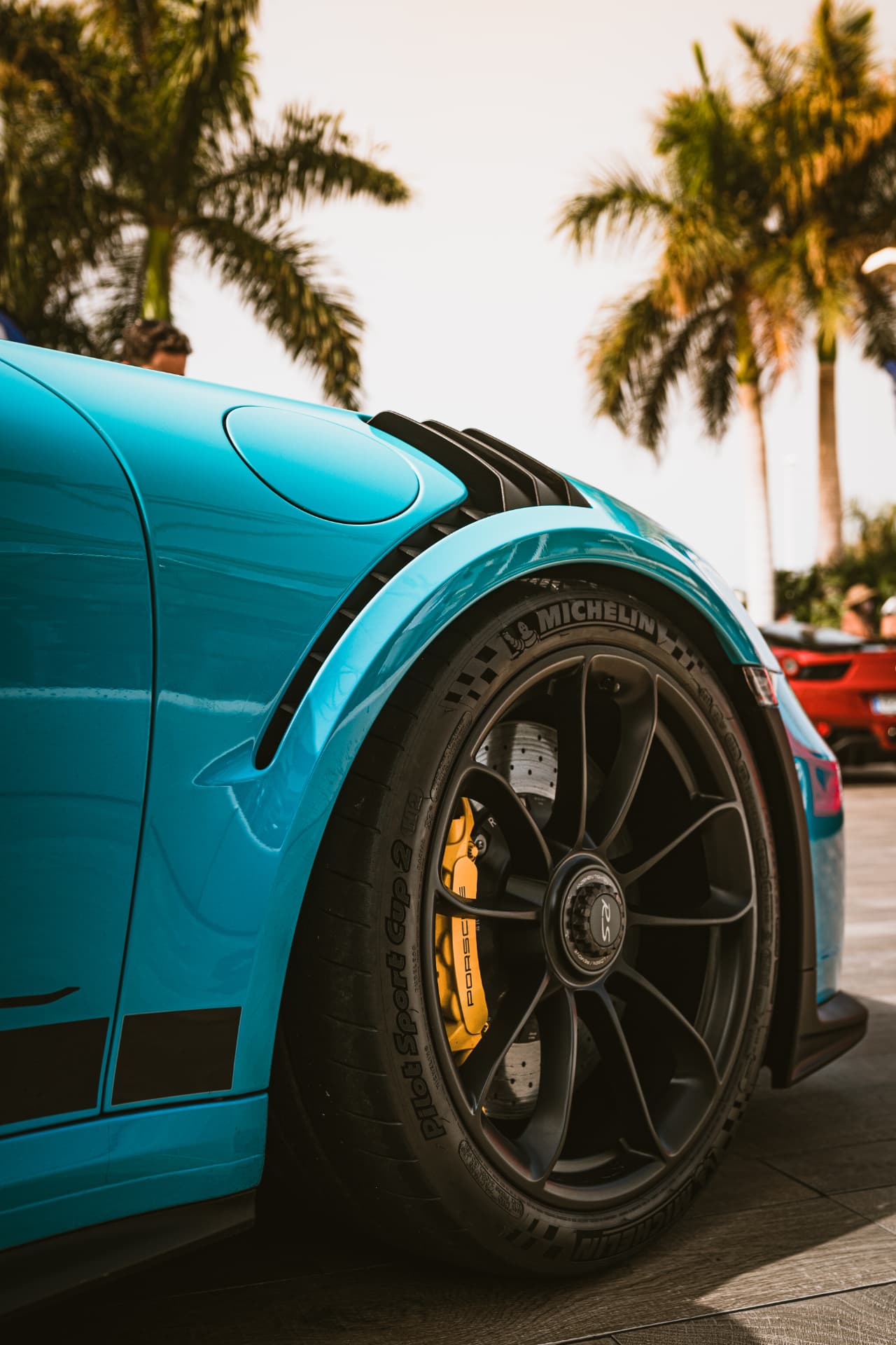 Detalle de la rueda de un Porsche turquesa con palmeras al fondo, fotografía de automoción